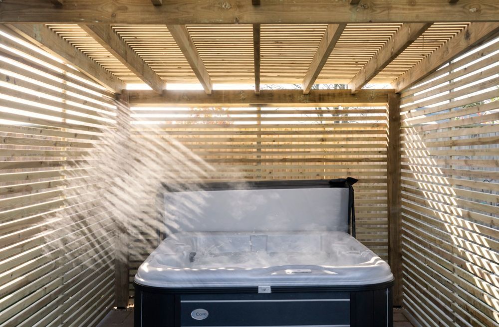A hot tub is sitting under a wooden pergola with steam coming out of it in a Retrofit Consultancy in Battle
