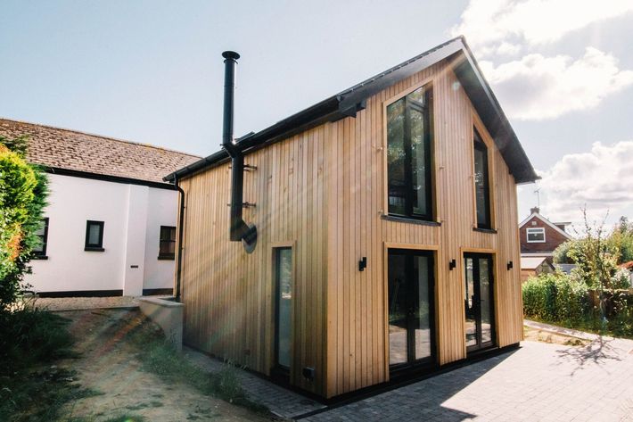 A house with a brick wall and a white roof is sitting on top of a lush green hillside in East Sussex Passivhaus in Hastings