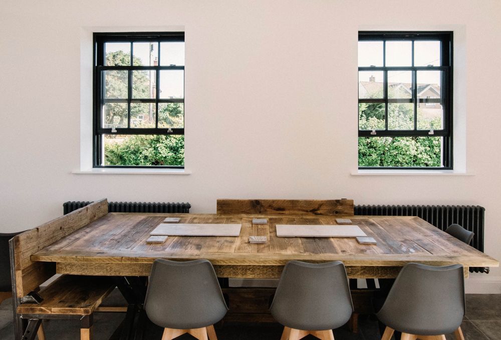 A wooden table and chairs in a room with two windows in a Retrofit Consultancy in East Sussex