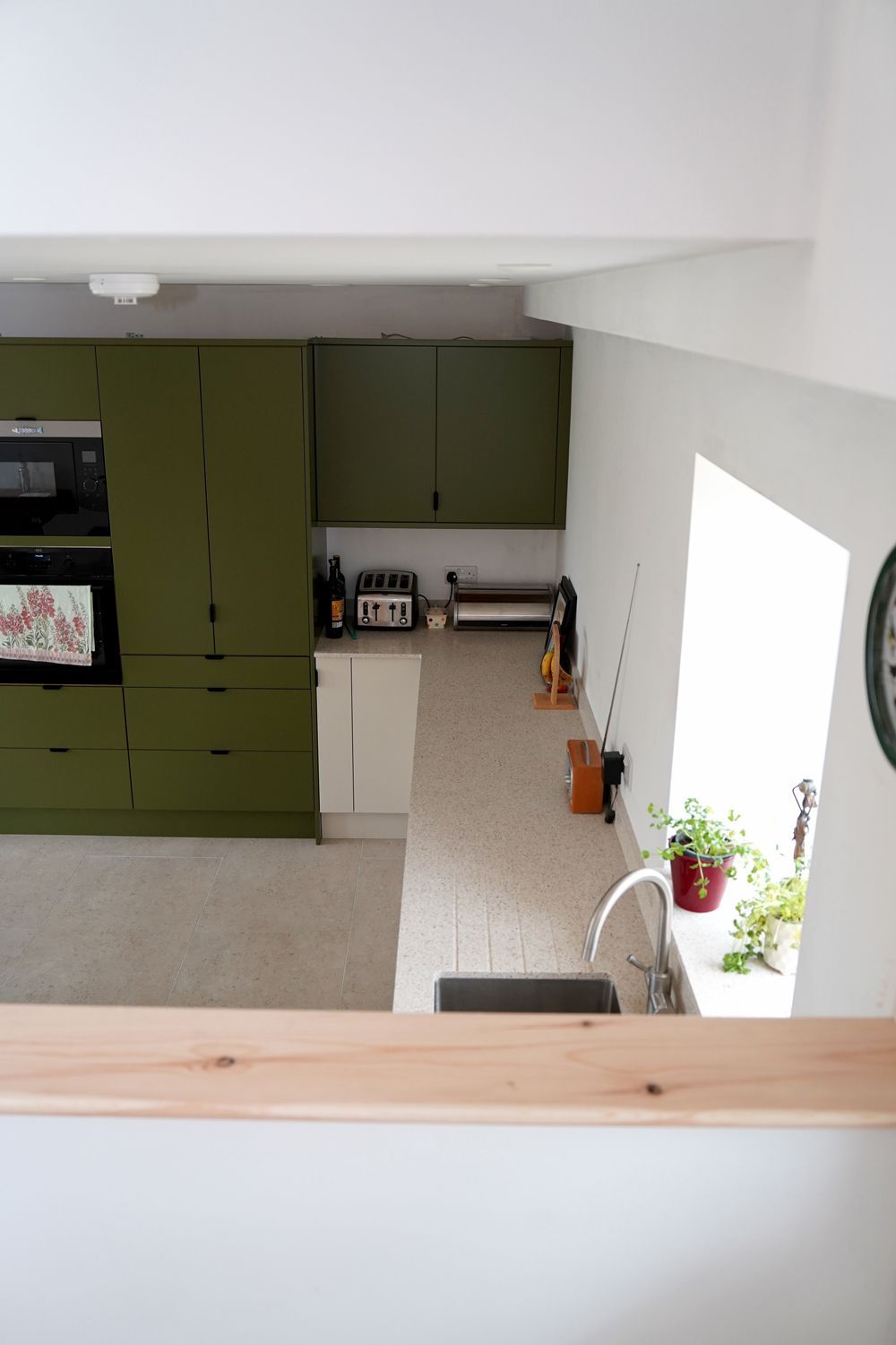 A kitchen with green cabinets and a clock on the wall  in a Construction Management in East Sussex