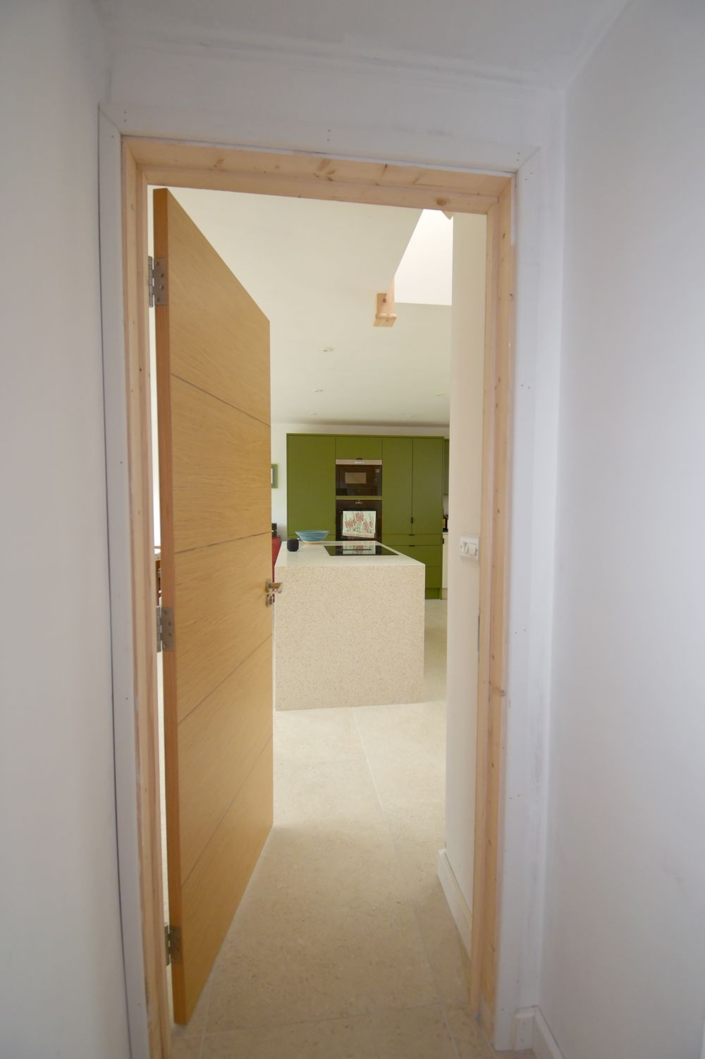 A hallway with a wooden door leading to a kitchen  in a Large-Scale Retrofitting in East Sussex