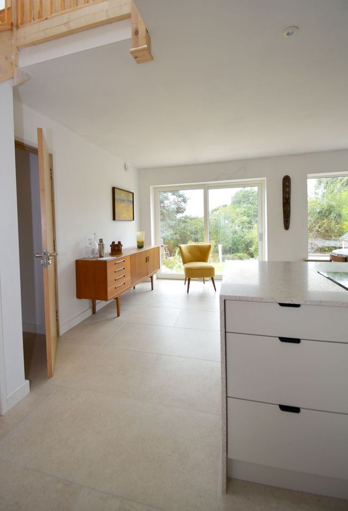 A kitchen with white cabinets and a yellow chair  in a Passivhaus new build in East Sussex