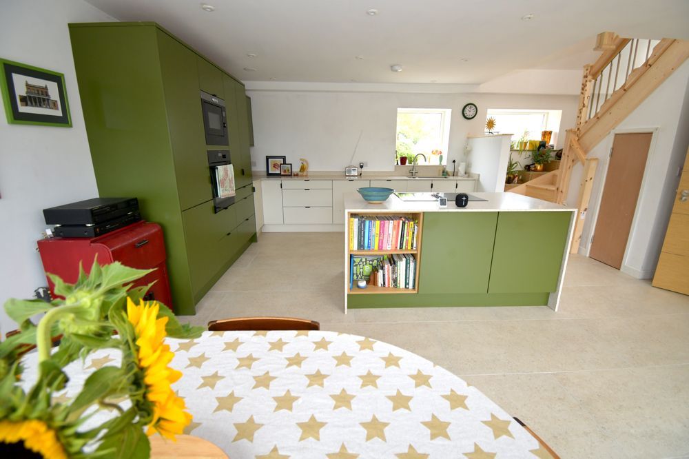 A kitchen with green cabinets and a table with a sunflower on it  in a Passivhaus New Builds in East Sussex