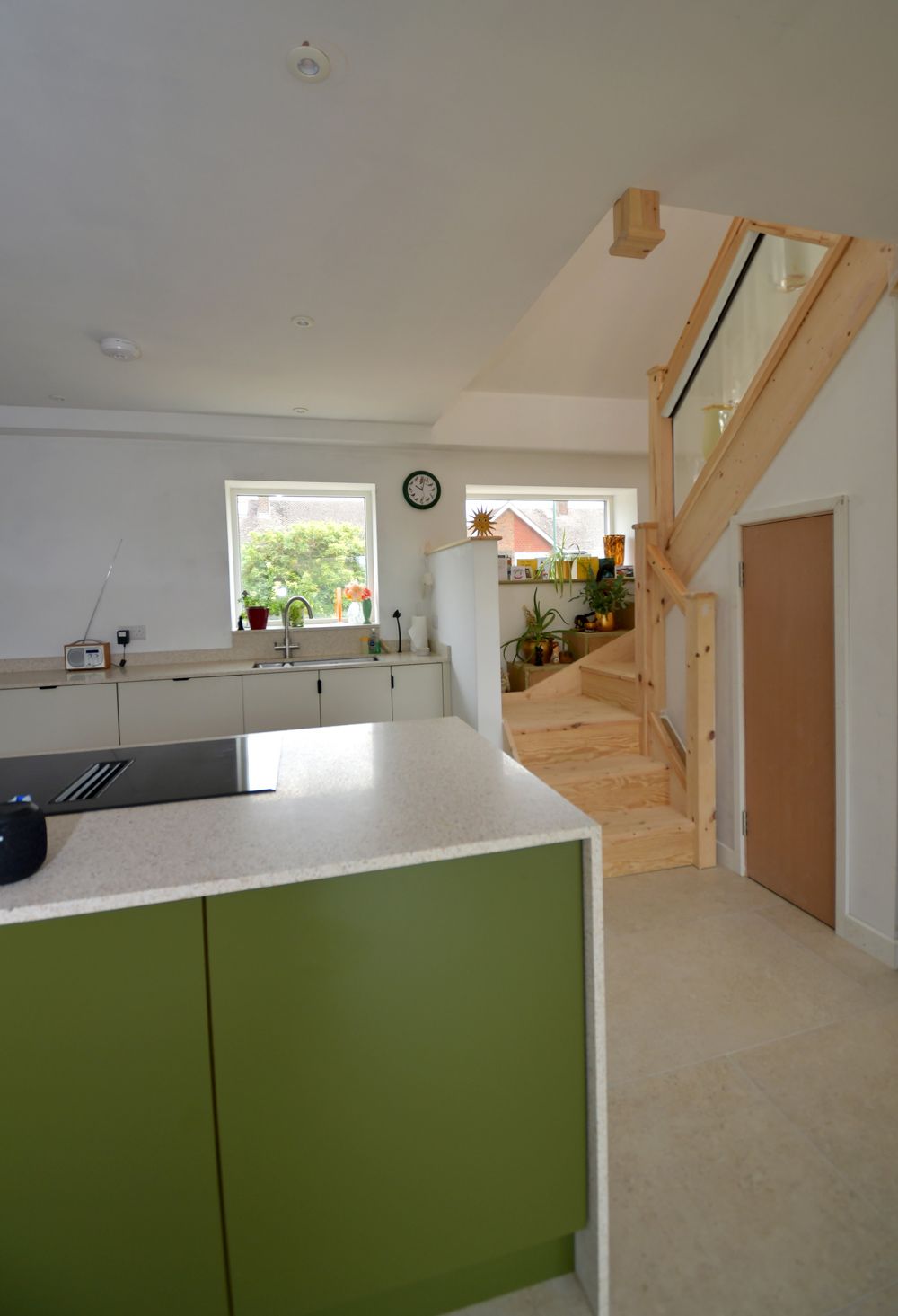 A kitchen with green cabinets and a wooden staircase  in a Passivhaus New Builds in East Sussex