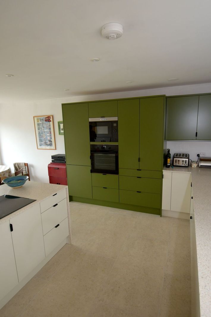 A kitchen with green cabinets and white counter tops in a Large-Scale Retrofitting in East Sussex