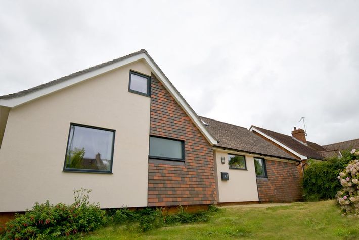 A house with a brick wall and a white roof is sitting on top of a lush green hillside  in East Sussex Passivhaus in Hastings