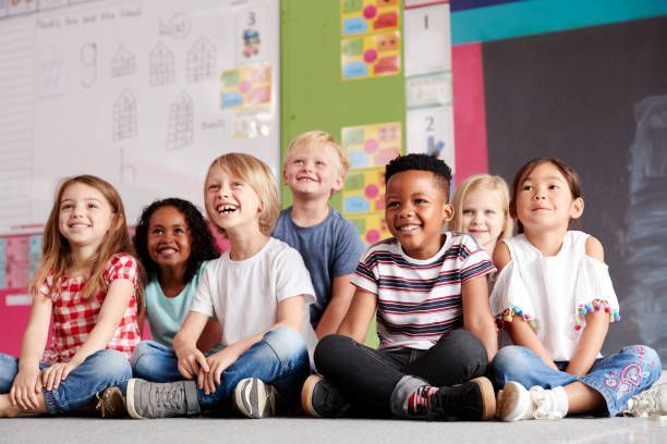 A group of children are sitting on the floor in a classroom.