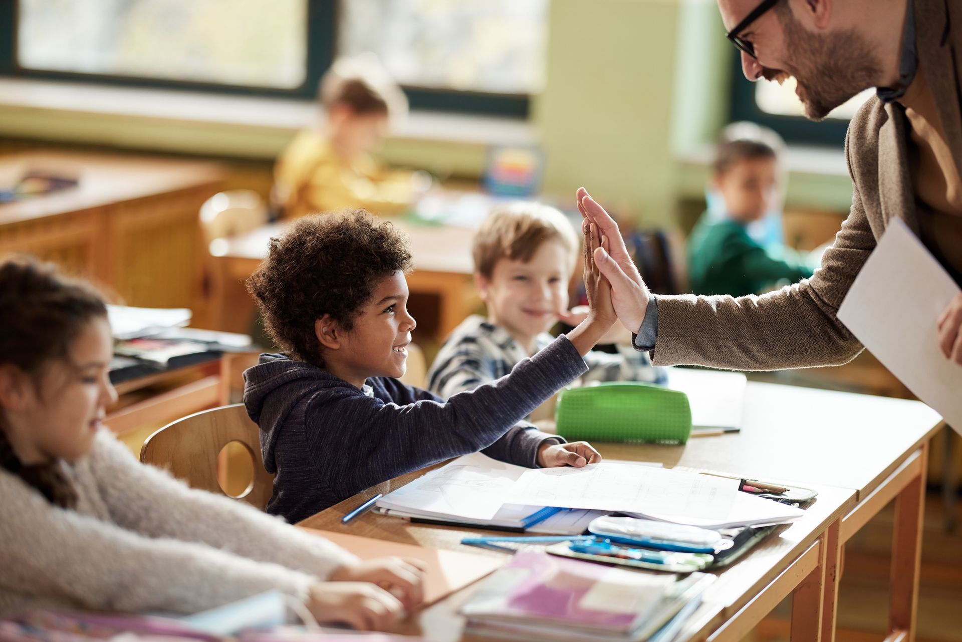 A teacher is giving a child a high five in a classroom.