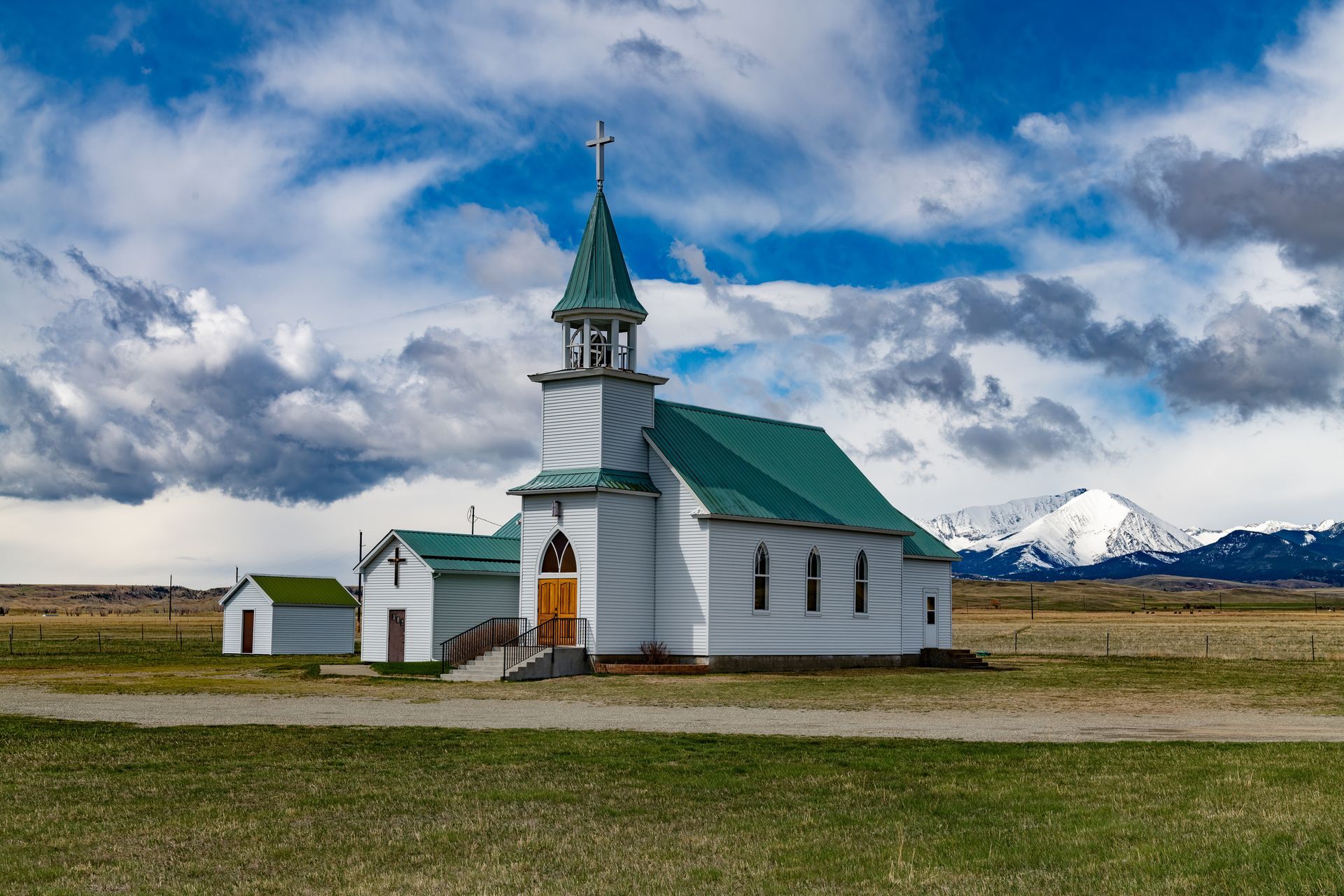 A small white church with a green roof is in the middle of a grassy field.