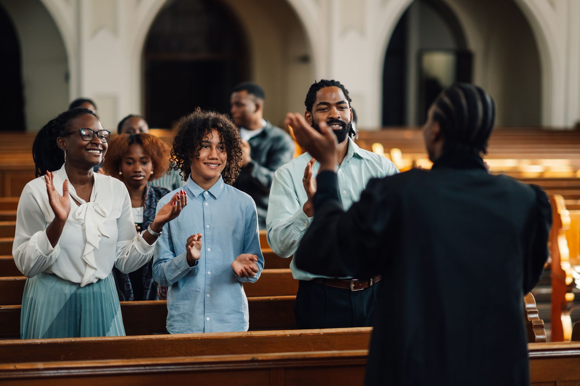 People clapping in church; a woman in a robe faces them from the front.