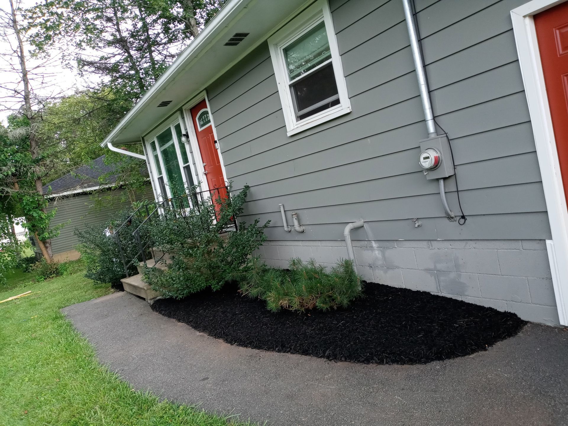 a gray house with a red door and black mulch in front of it .