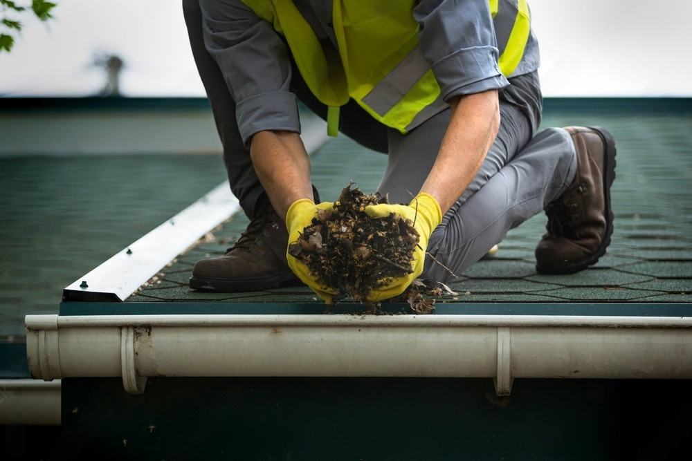 a man is kneeling down on a roof holding a pile of dirt .