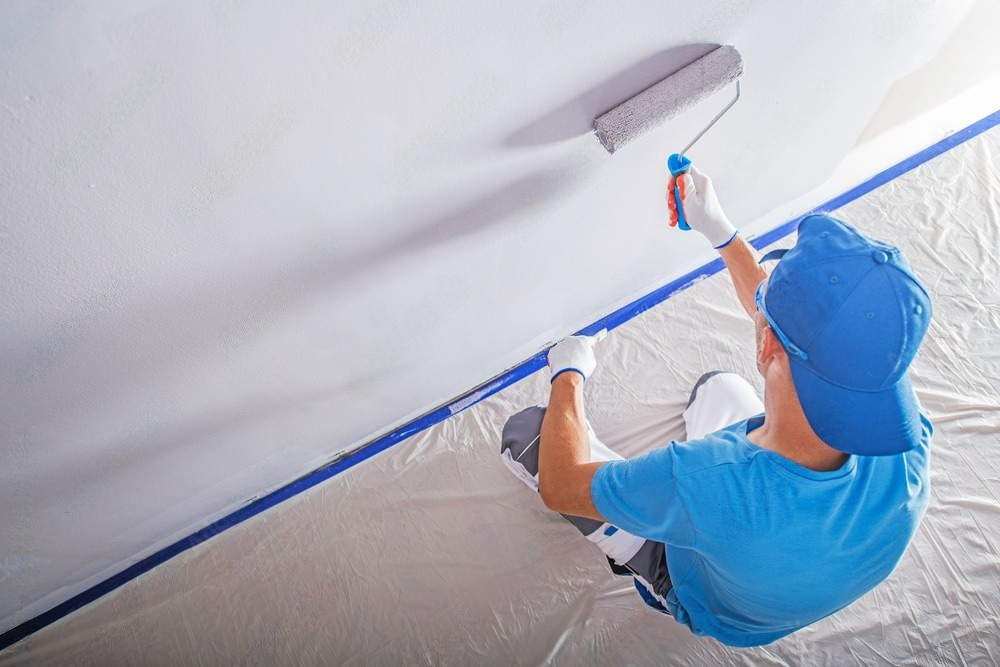 a man is sitting on the floor painting a wall with a roller .