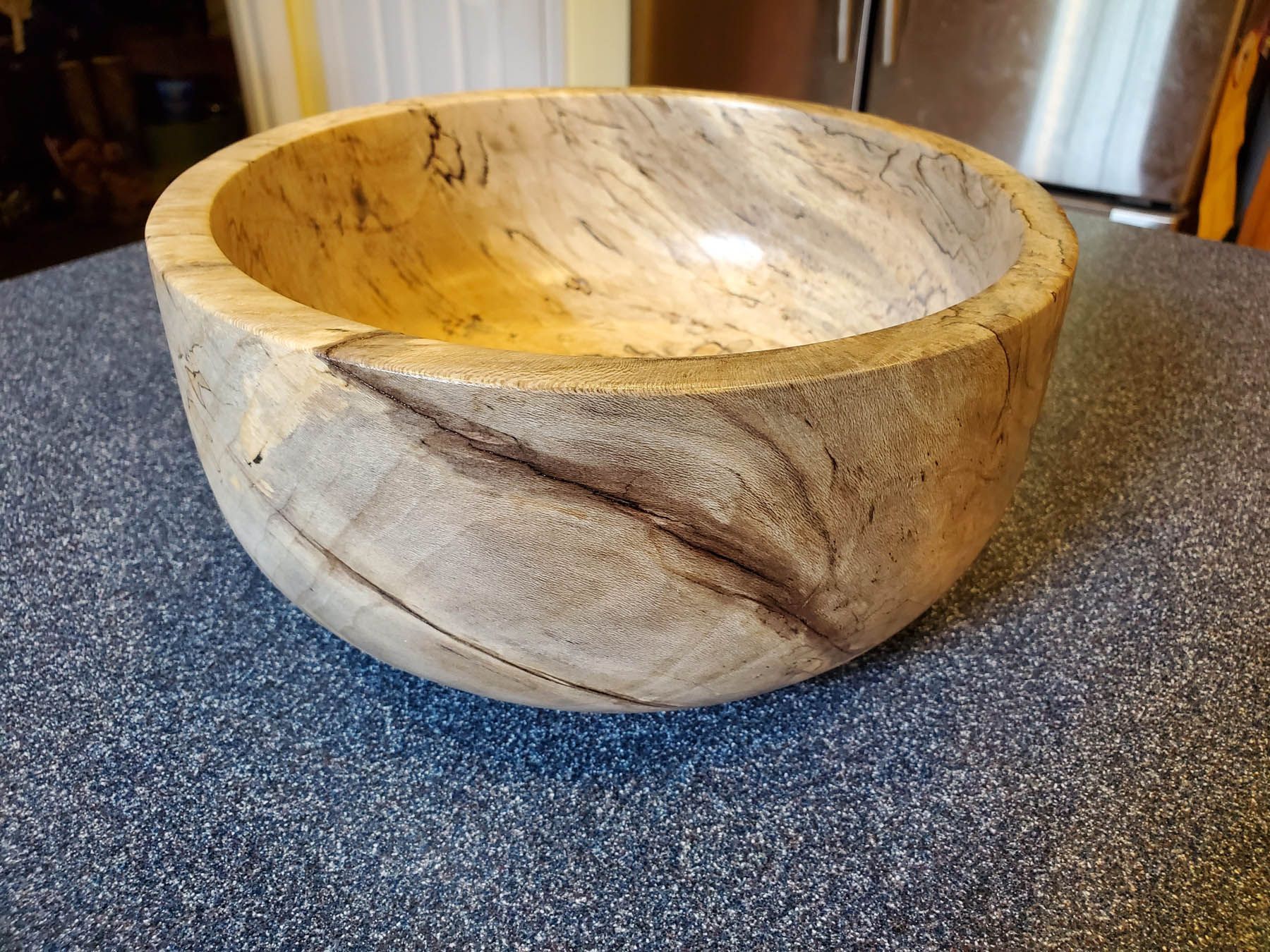 Wooden bowl with natural grain and dark streaks on a blue speckled surface.