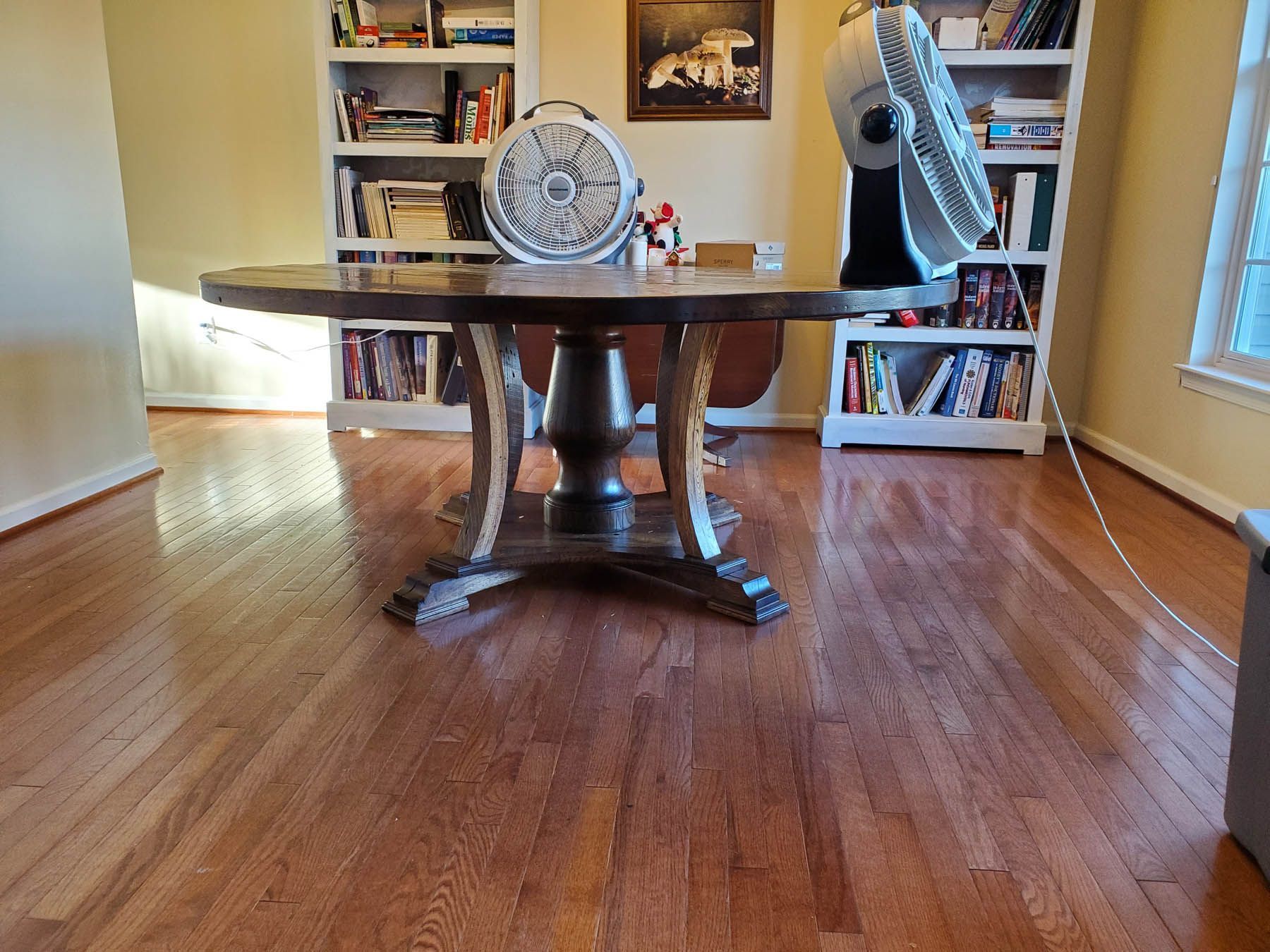 Wooden table with fan on top in a room with bookshelves and hardwood floors.