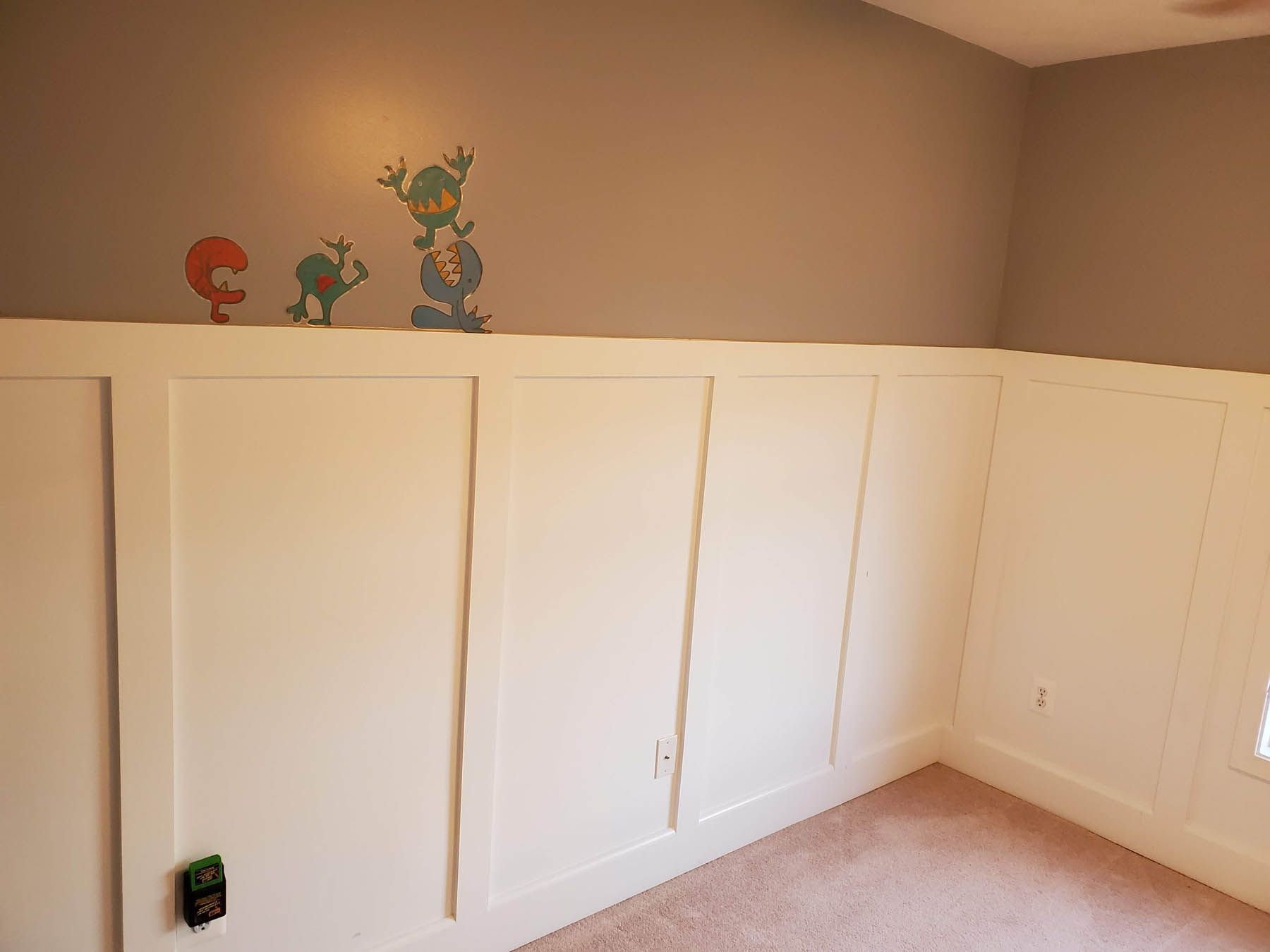 White wainscoting with a muted grey wall above it. Colorful cartoon characters are on the wall.