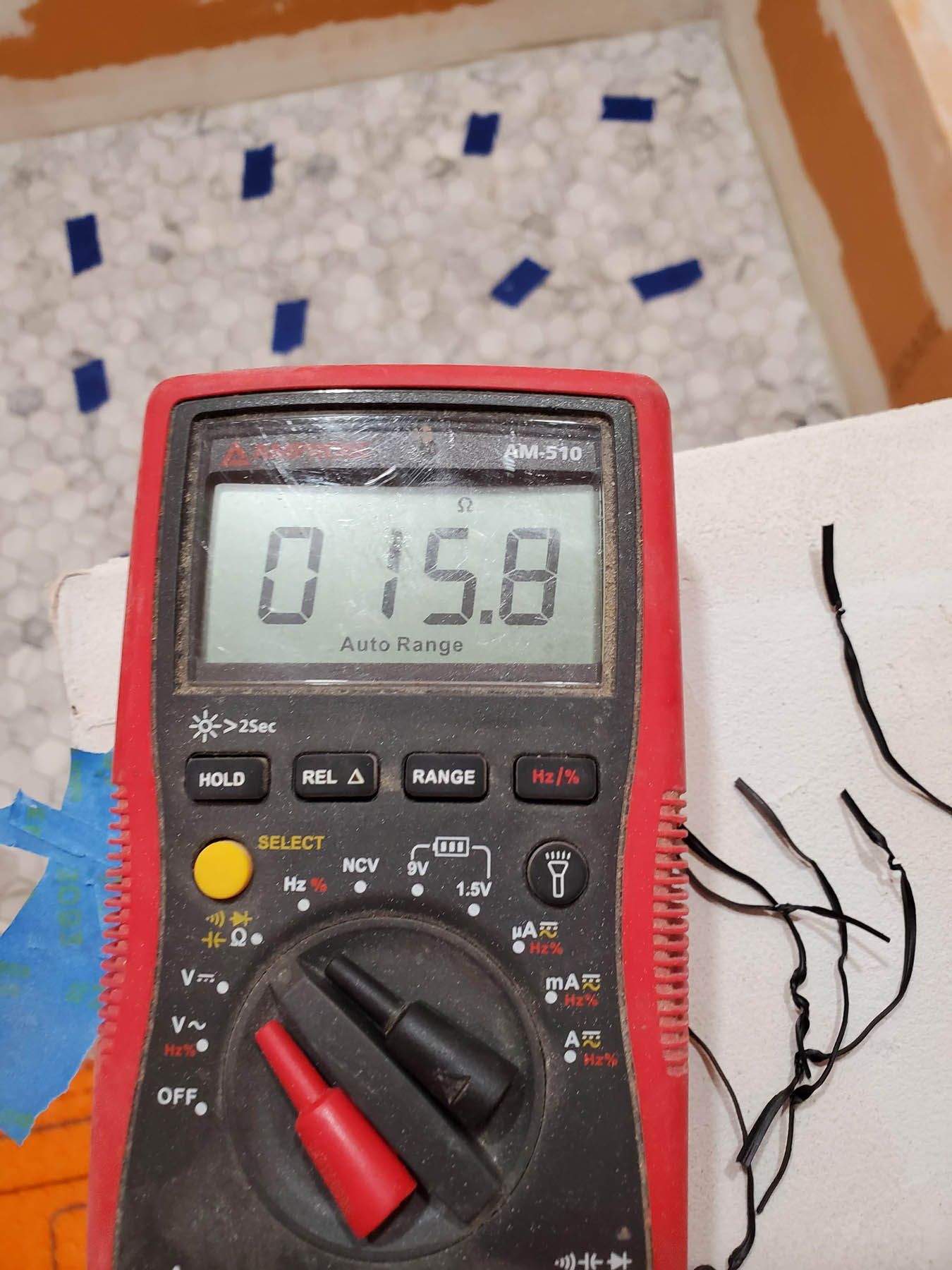 Multimeter displays 15.8. Probes connected to wires, tiles in background with blue tape.