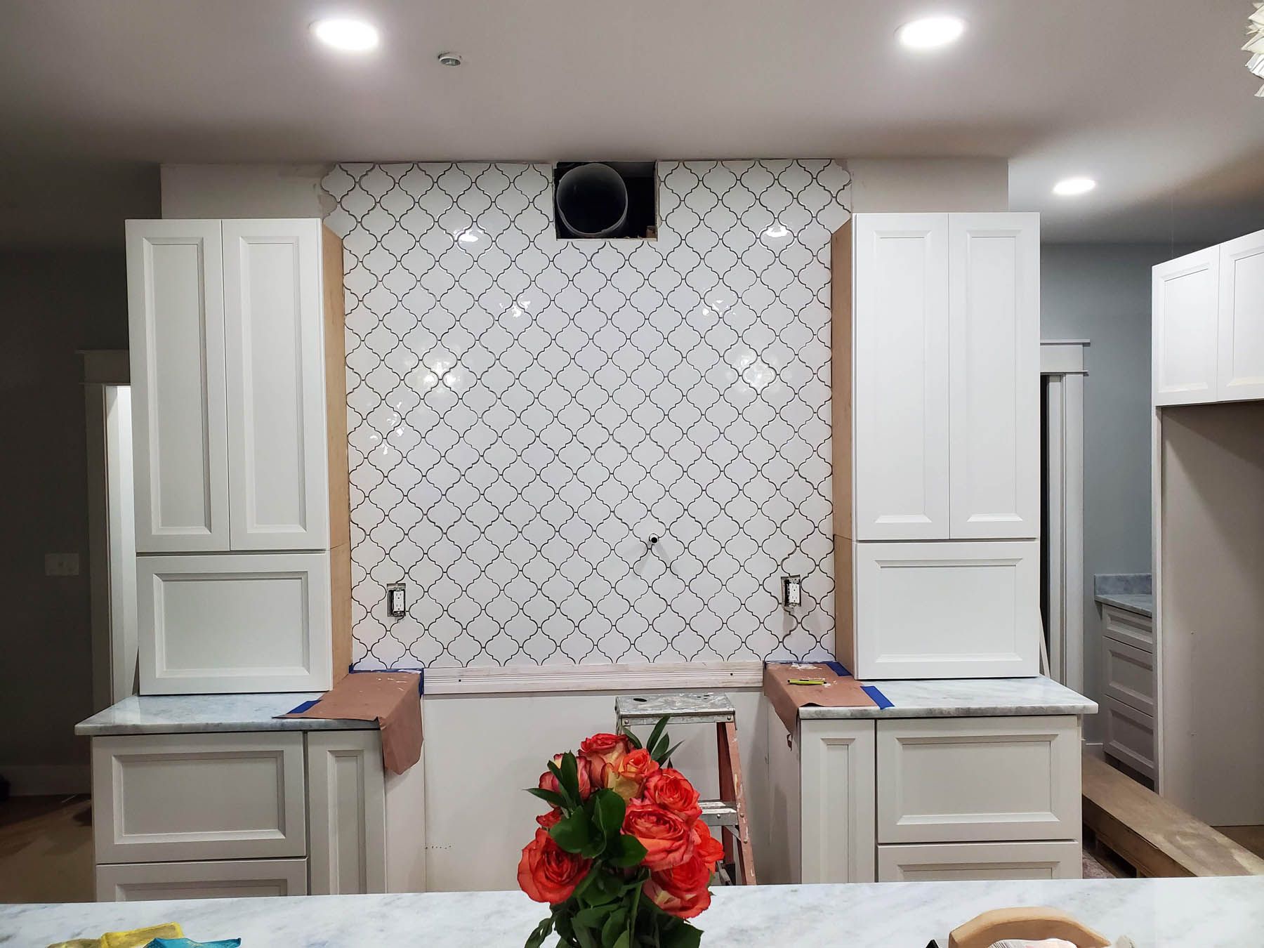 Kitchen renovation: white cabinets, patterned tile backsplash, centered range hood, flowers.