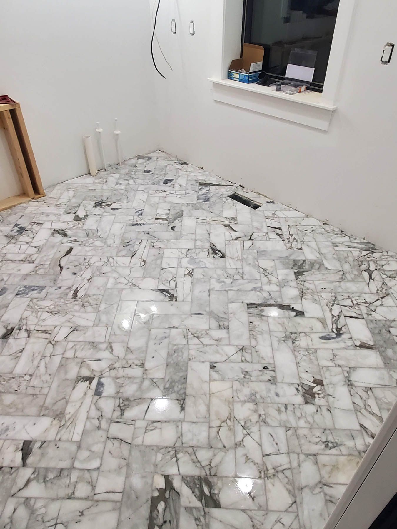 Marble tile flooring laid in a herringbone pattern in a room with white walls.