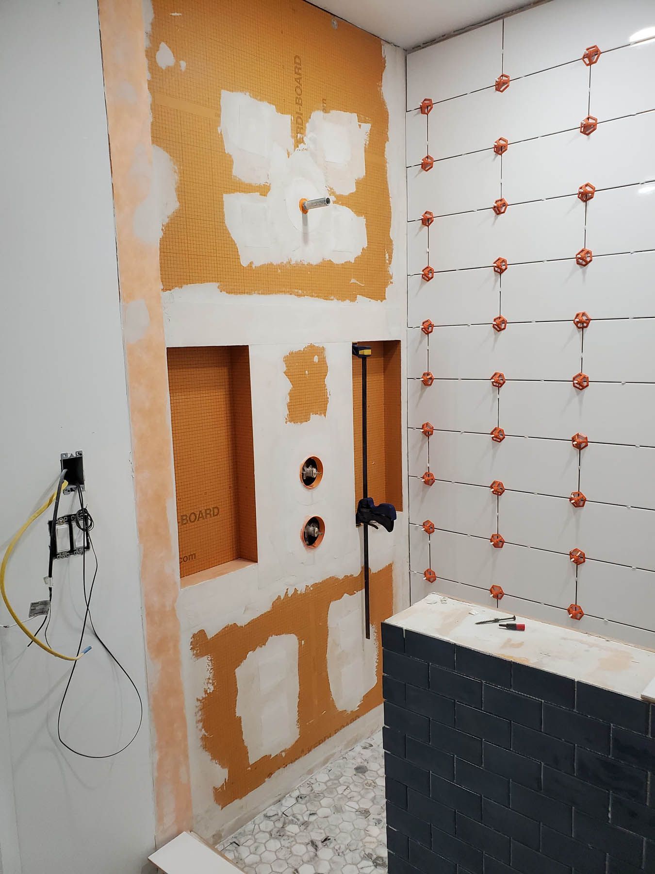 Bathroom under construction: Orange waterproof wall panels with niches, white tiled wall, plumbing, and tile leveling system.