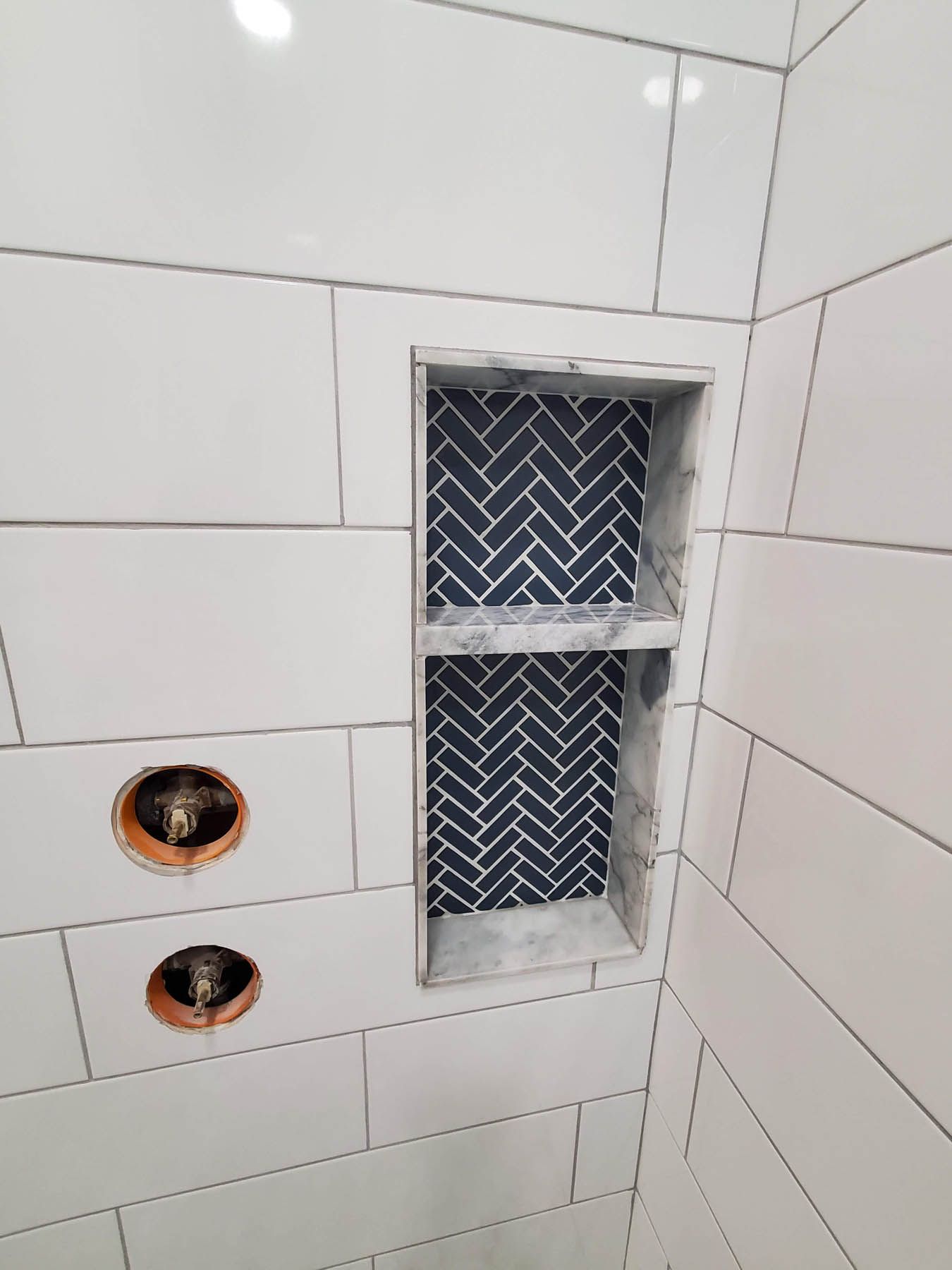 White tiled shower with a built-in shelf lined with herringbone pattern tiles.