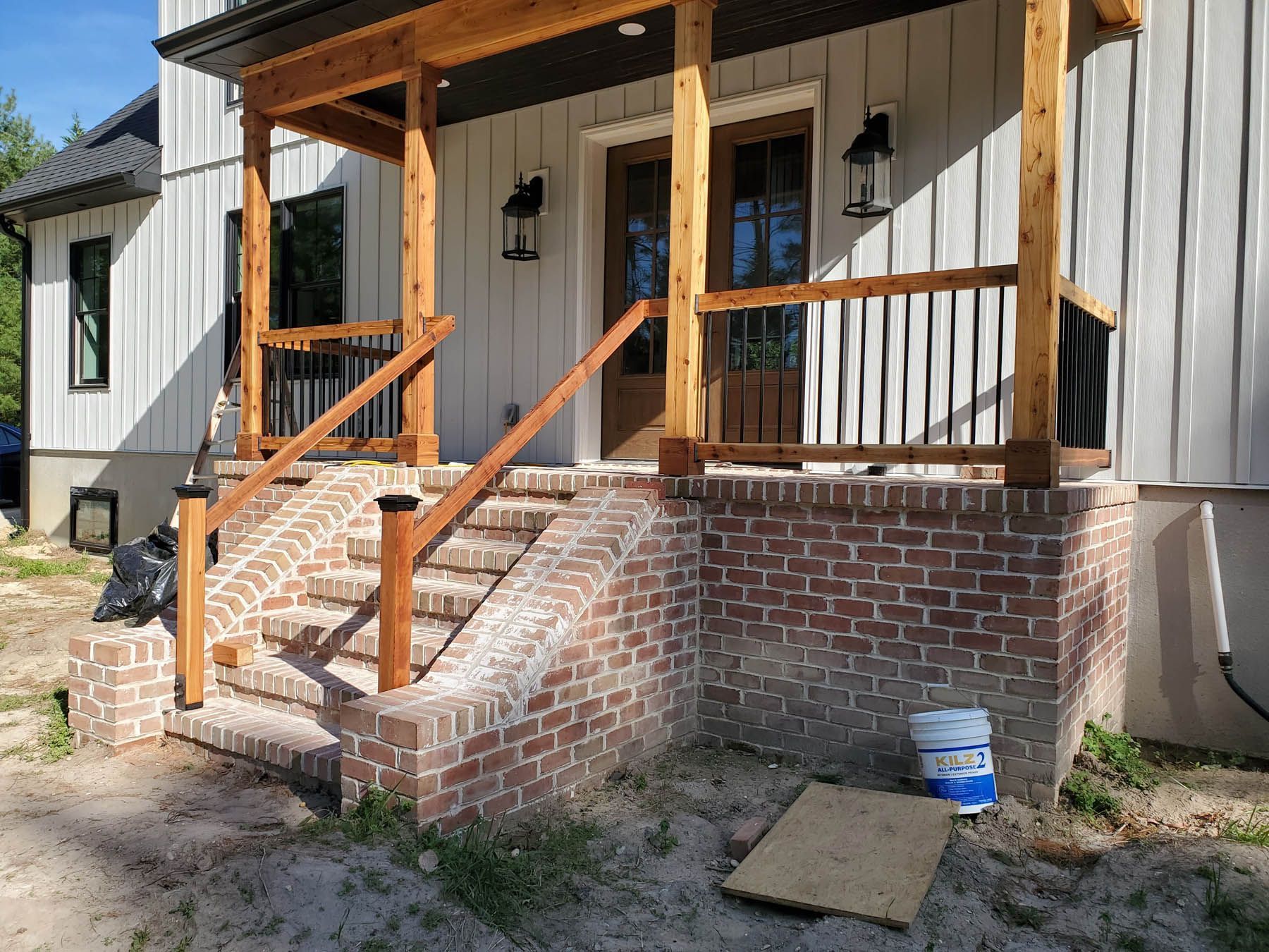Brick steps lead up to a porch with a wooden railing, and front door. The house has vertical siding.