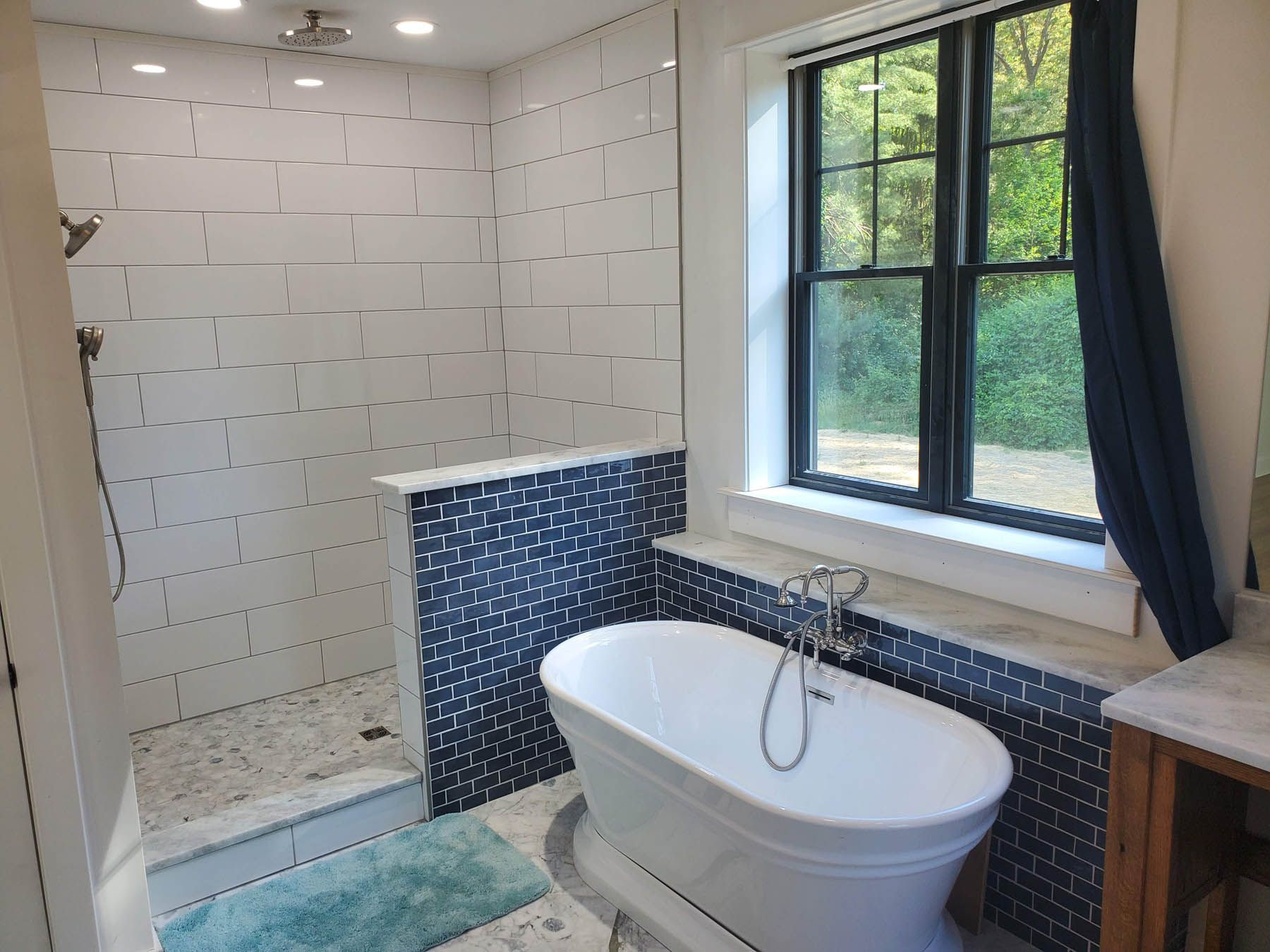 Bathroom with white and blue tile, standalone tub, shower, and window with curtain.