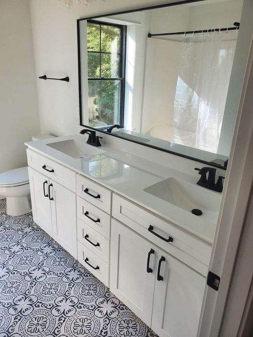 White bathroom with a double vanity, patterned floor, and a large mirror.