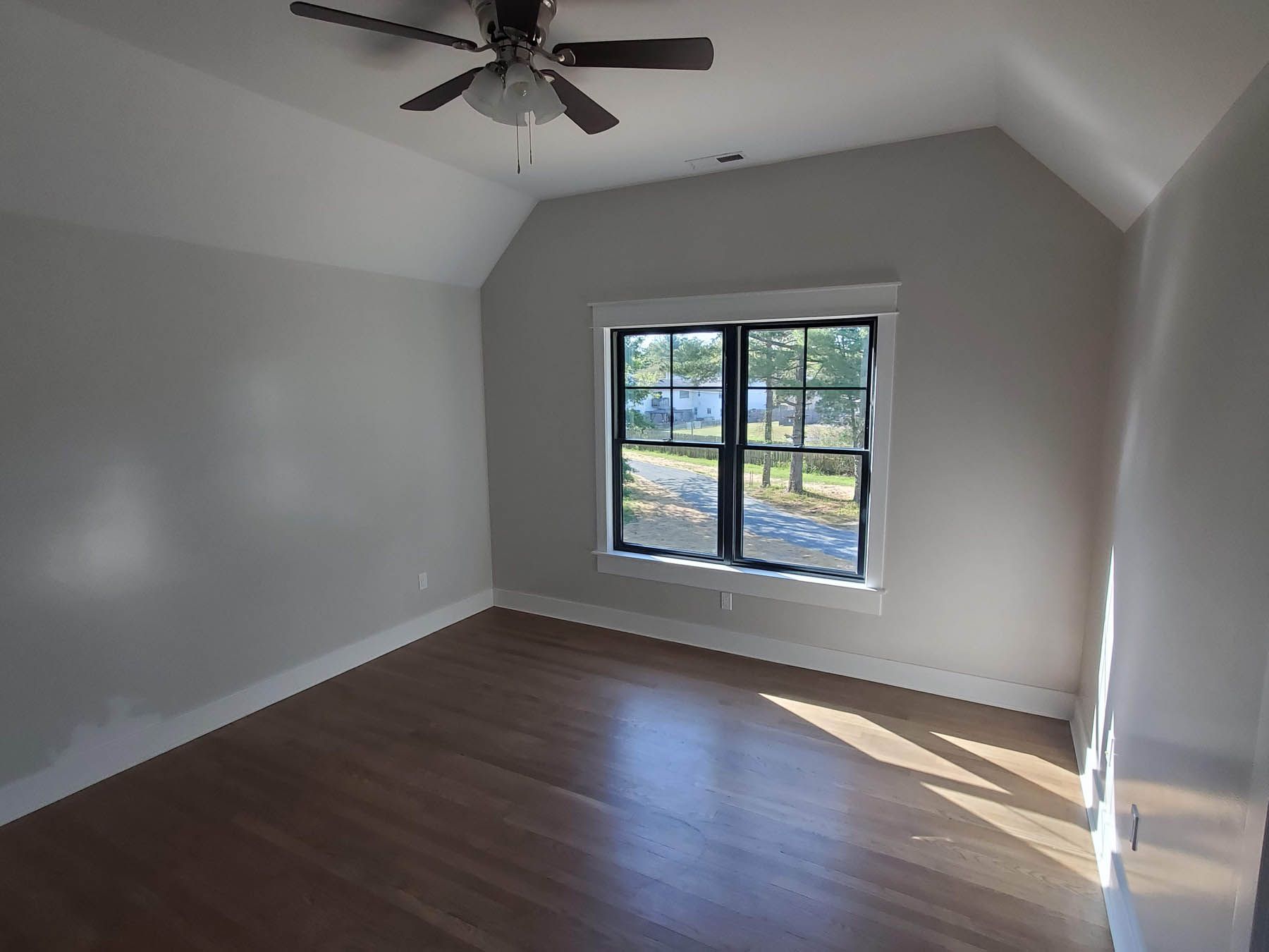 Empty room with hardwood floor, window, and ceiling fan.