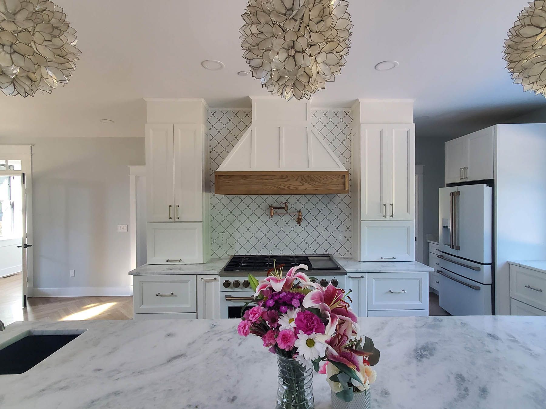 White kitchen with marble island, white cabinets, wooden range hood, and floral arrangement.