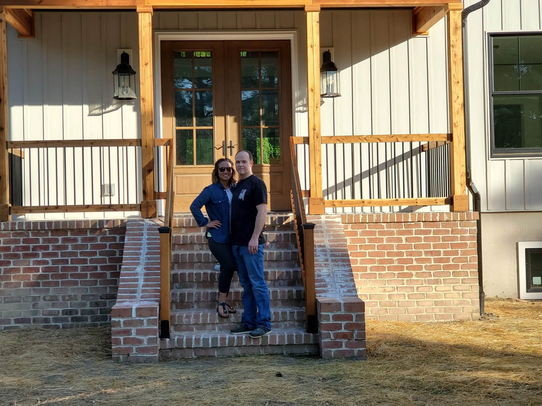 Couple standing on brick steps of a house with wooden door, under porch.