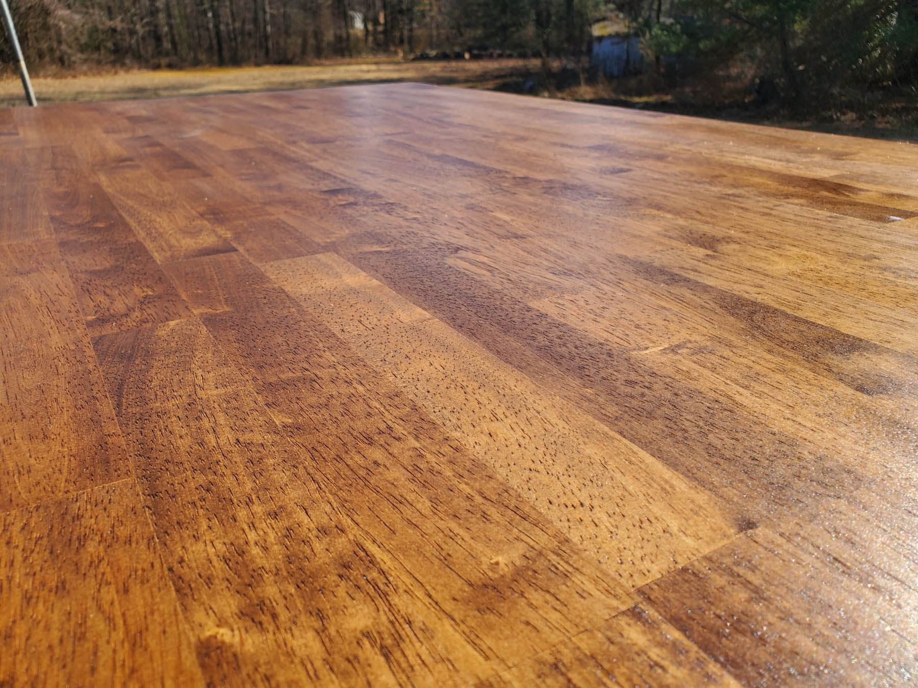 Close-up of a stained, wooden surface with visible grain and a glossy finish; outdoors.