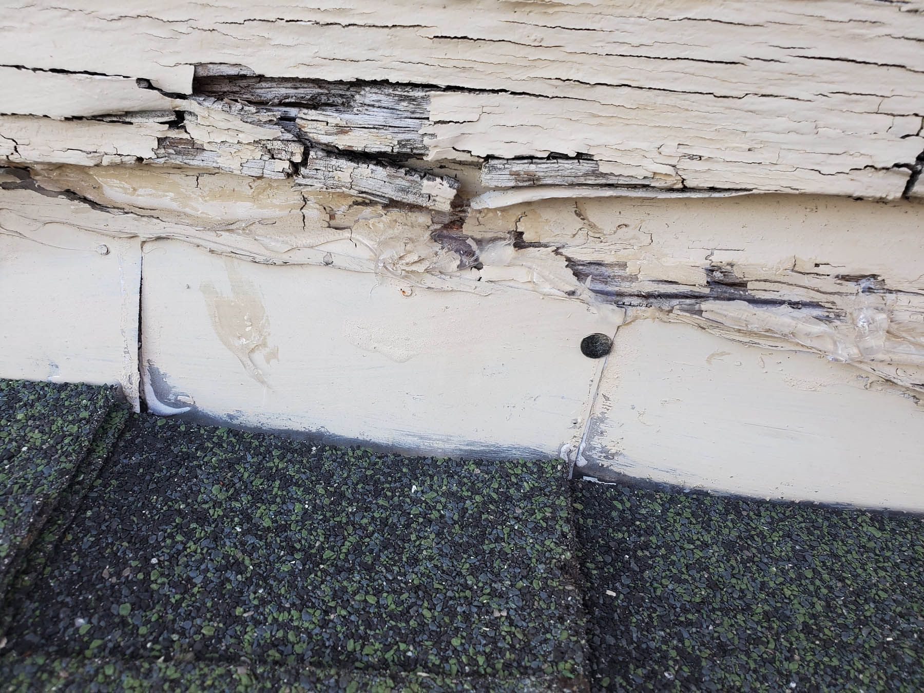 Damaged roof edge with rotted wood and a hole; shingles below.