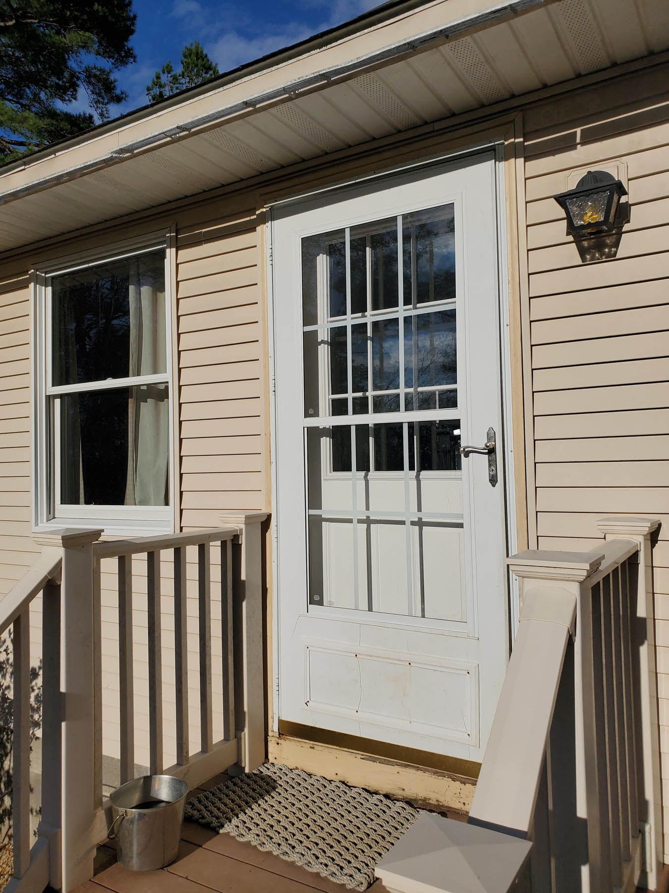 Exterior of a beige house with white-trimmed door and window; small porch with railing.