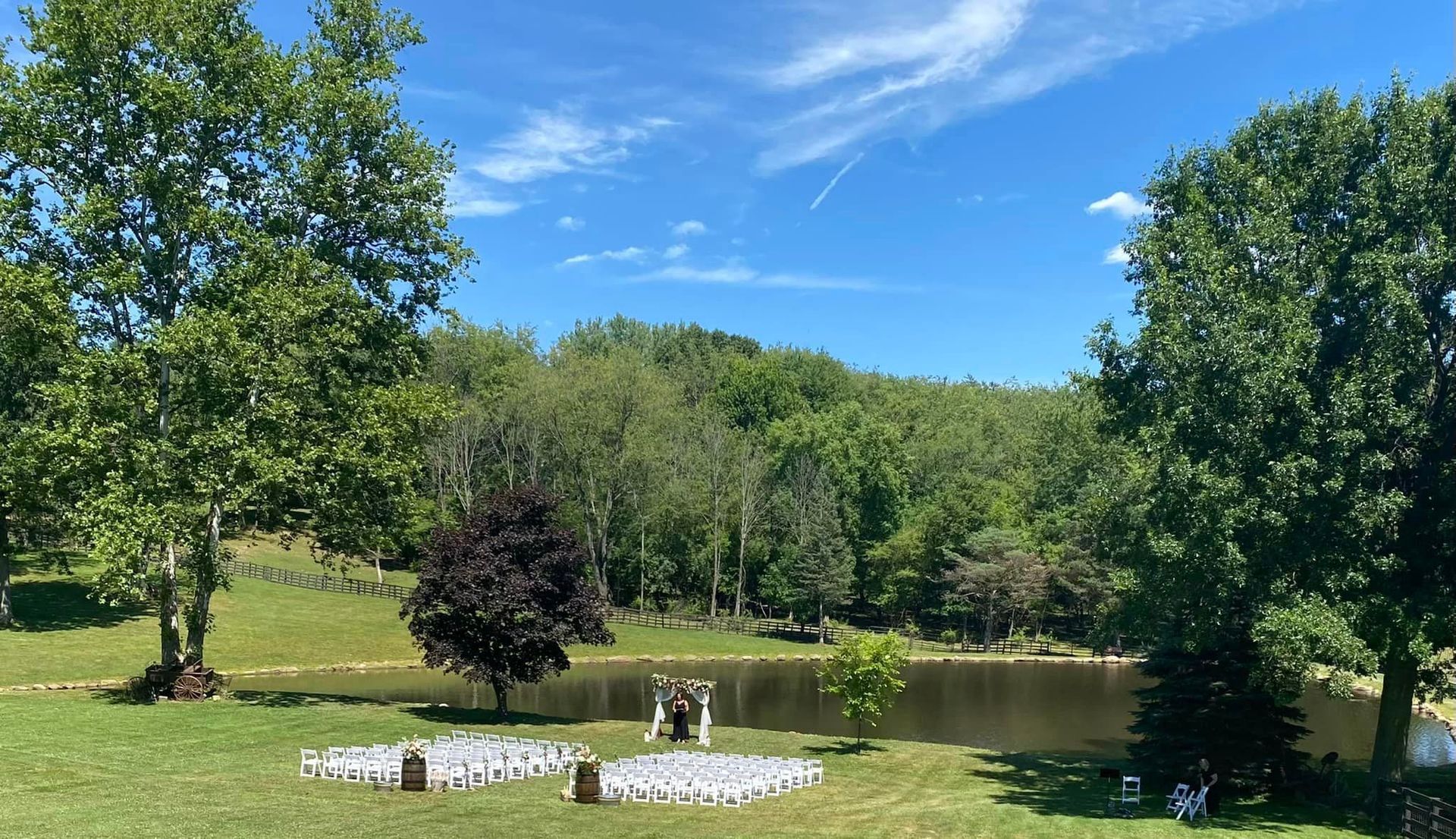 A wedding ceremony is taking place in front of a lake surrounded by trees.