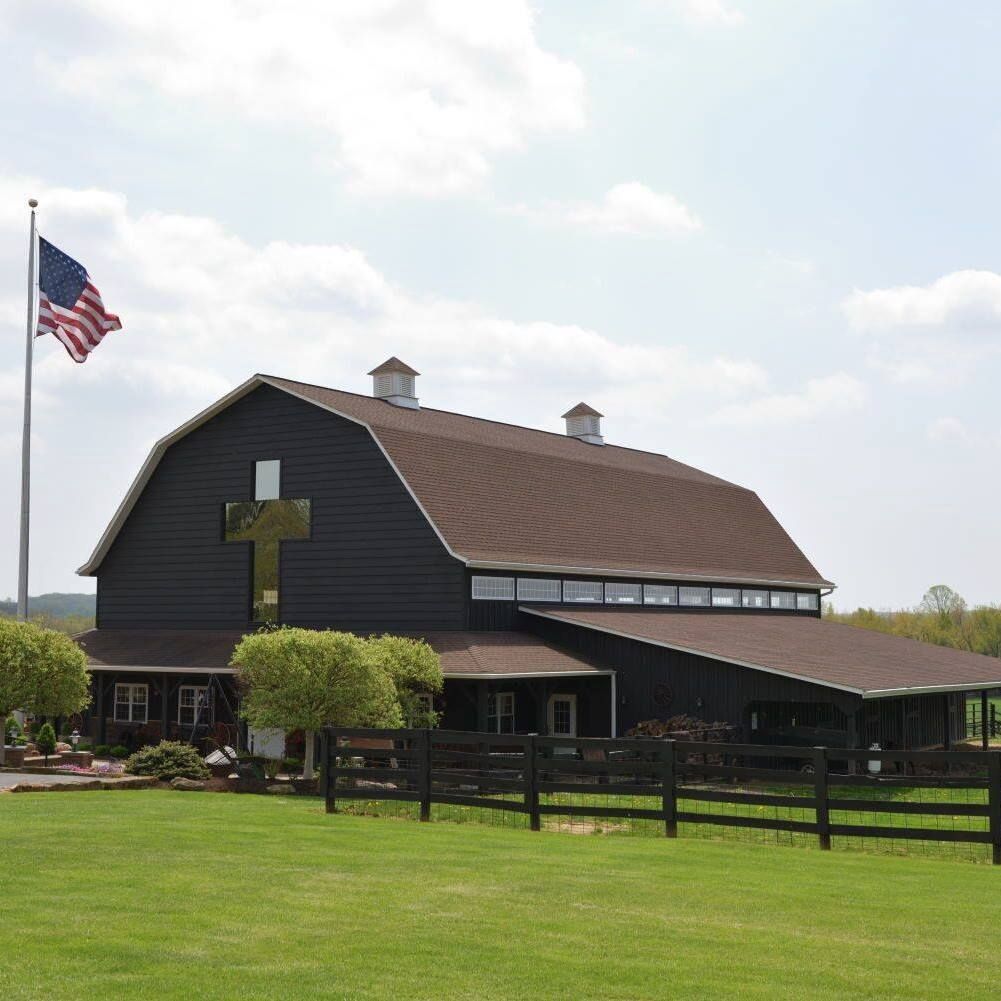 A black barn with a cross on the side and an american flag flying in front of it