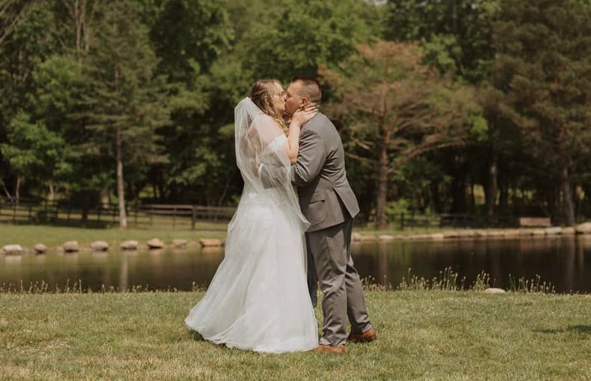 A bride and groom are kissing in front of a lake.