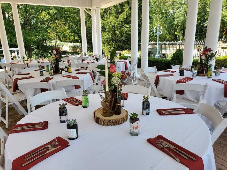 Tables set for an outdoor event under a white gazebo. Centerpieces include succulents, flowers, and candles.
