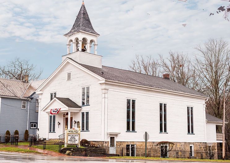 White church with steeple and bell tower; brick foundation and sidewalk.