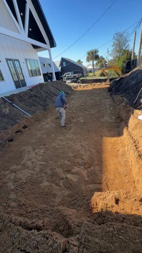 A person stands in a large, deep construction excavation for an inground pool next to a modern white house.