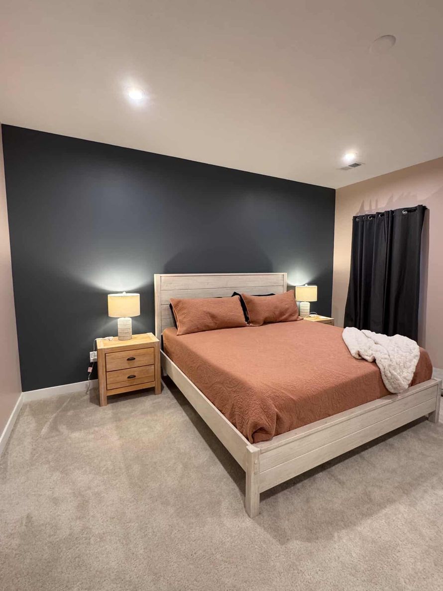 Bedroom with queen bed and two matching nightstands, charcoal accent wall, beige carpet.