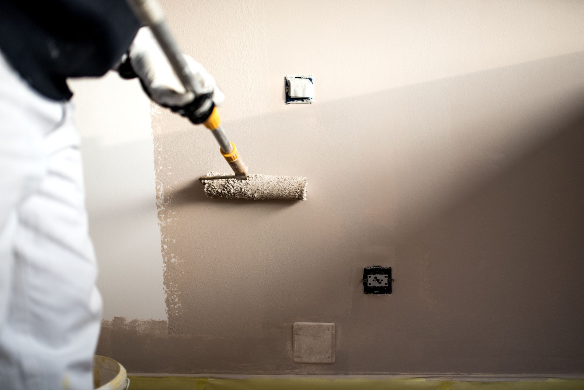A painter is rolling light gray paint onto an interior wall.