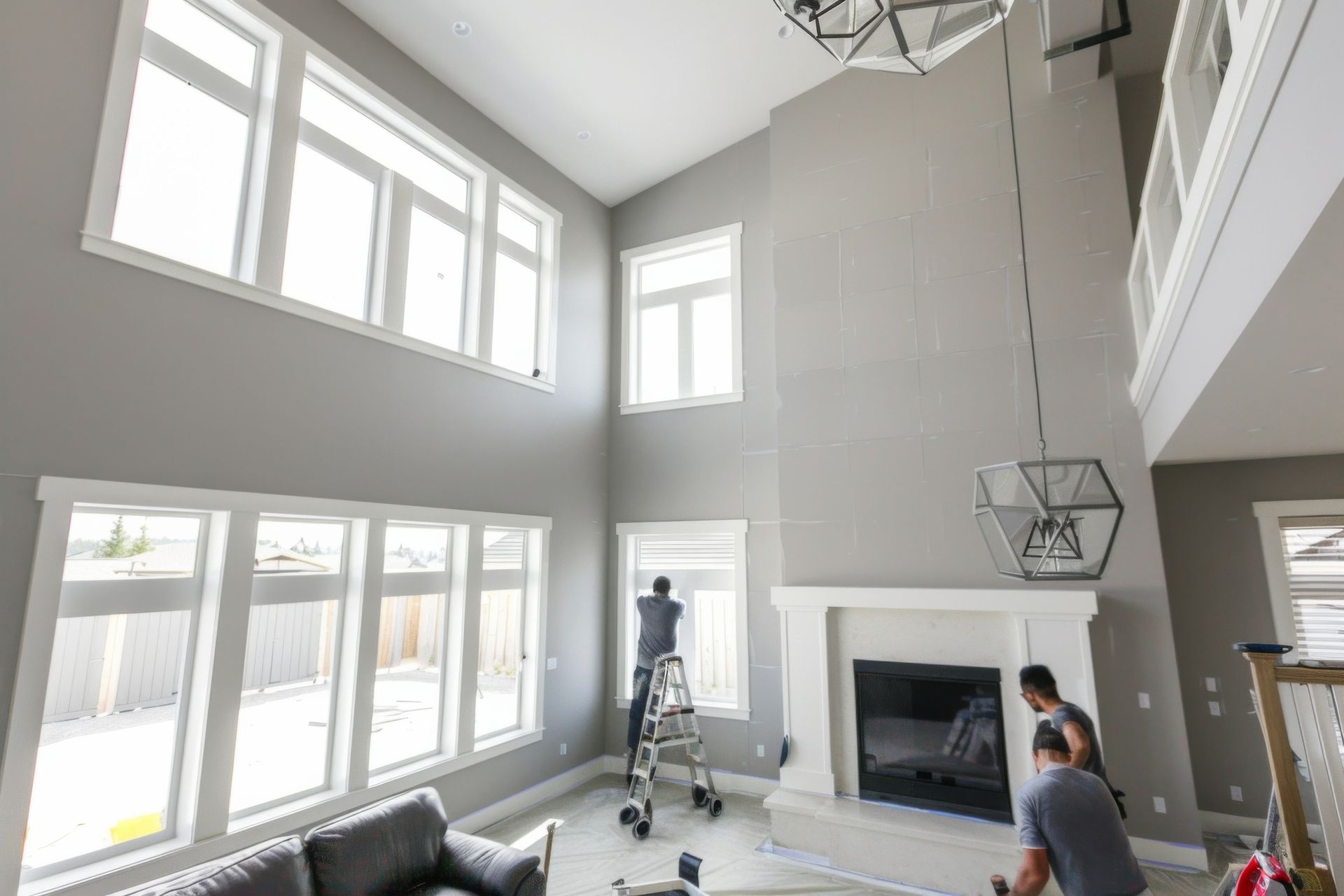 Two male workers painting light gray walls in a modern home’s spacious living room.