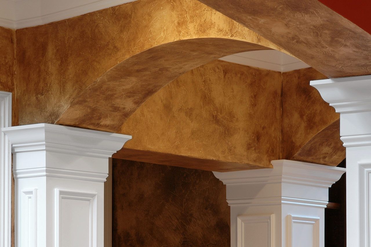Arched doorway with textured brown and gold walls, supported by white pillars.