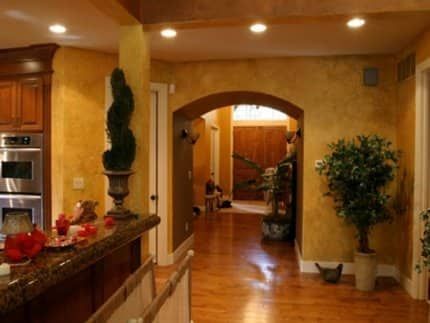 Interior of a home with arched doorways, warm yellow walls, wood floors, and potted plants.
