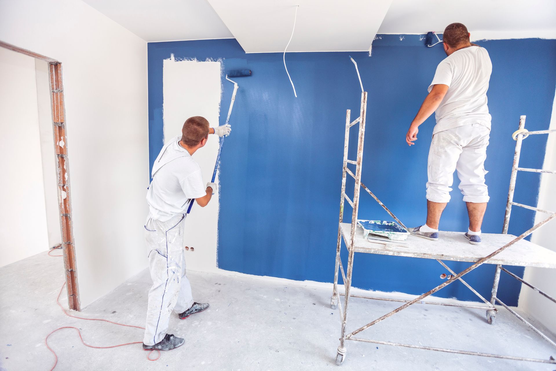 Professional painters applying white and blue paint on interior walls during home renovation.