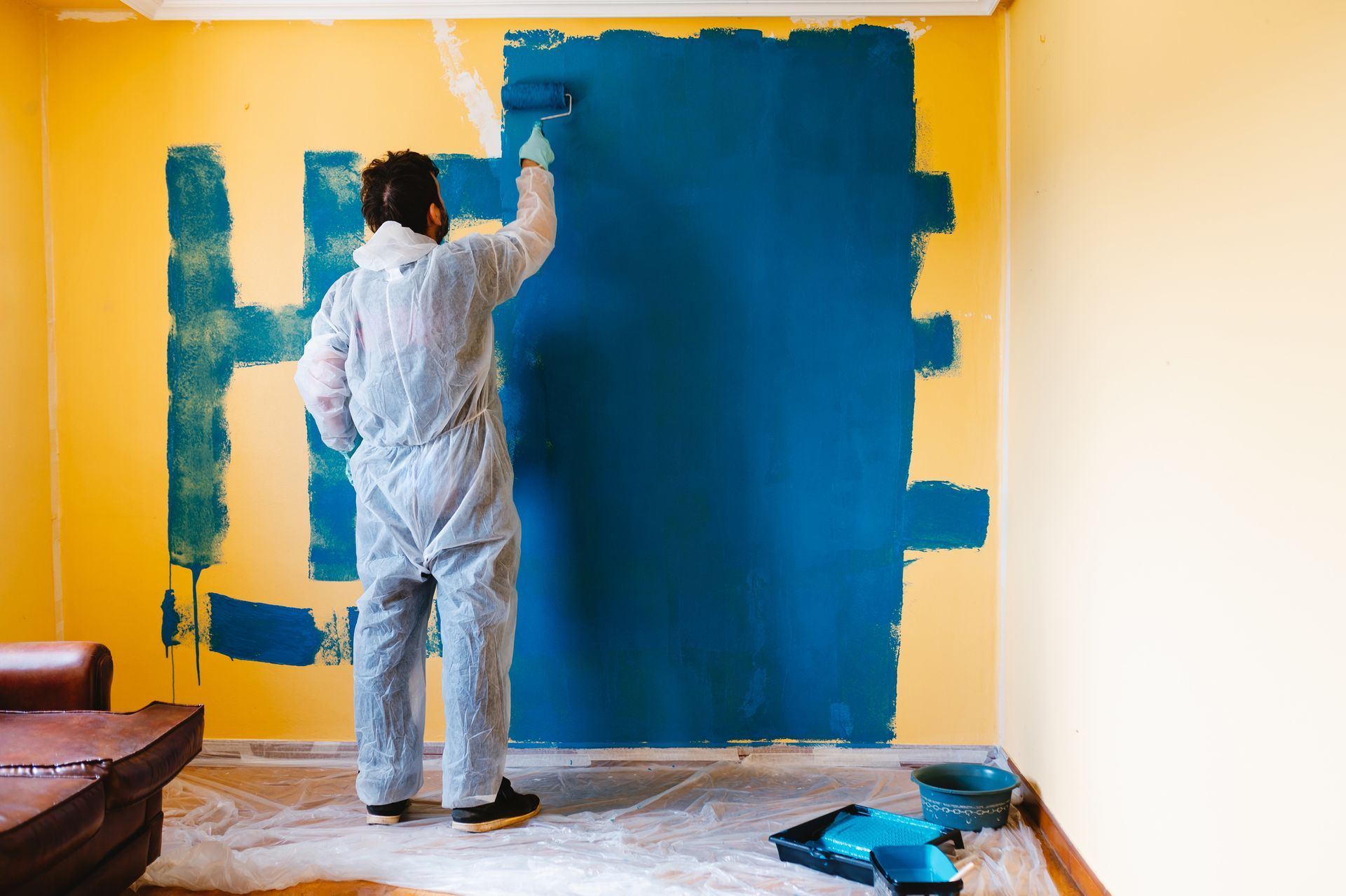 A male painting contractor applies a coat of blue paint to a wall inside a room. A male painting contractor applies a coat of blue paint to a wall inside a room.
