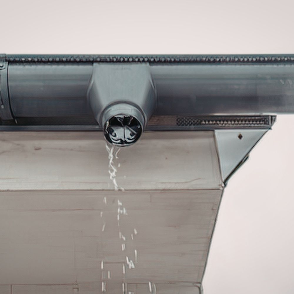 Water drips from an open, dark gray gutter outlet attached to the edge of a roof.