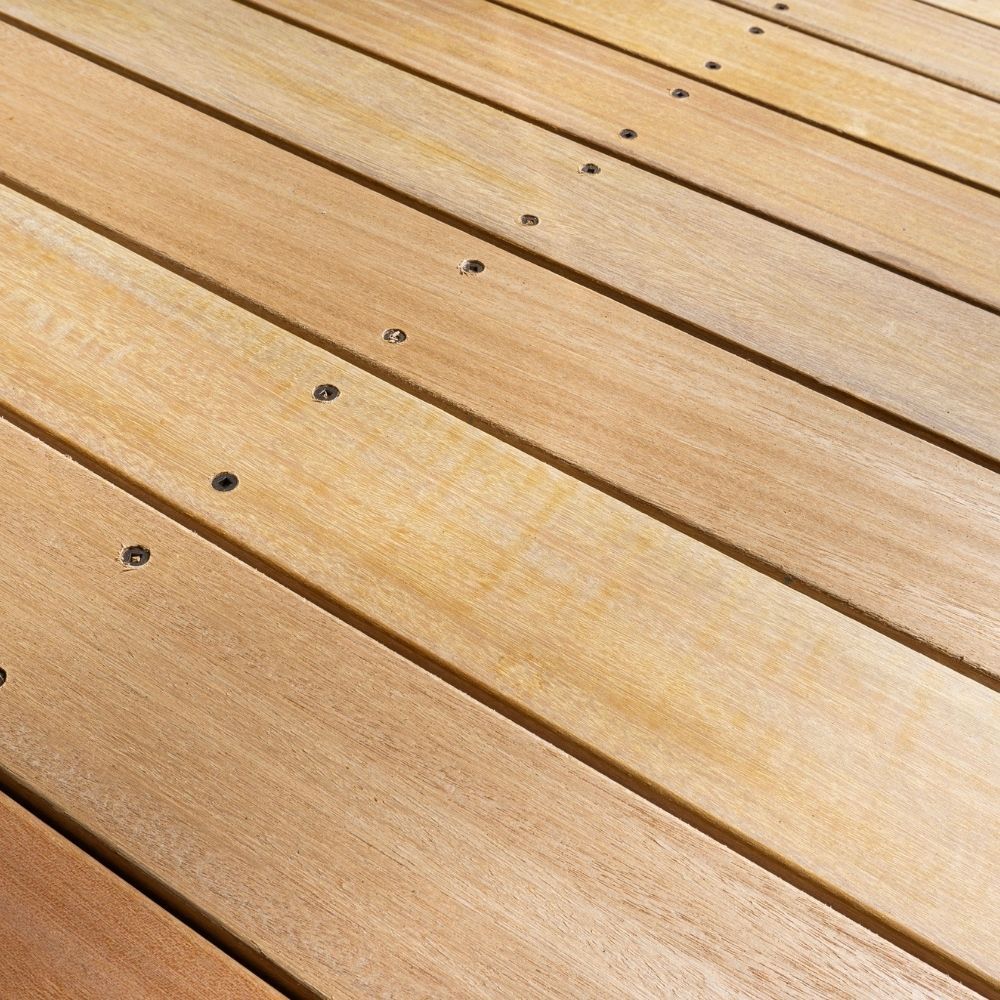 A close-up of light-colored wooden deck planks installed in parallel with metal screws securing each board.