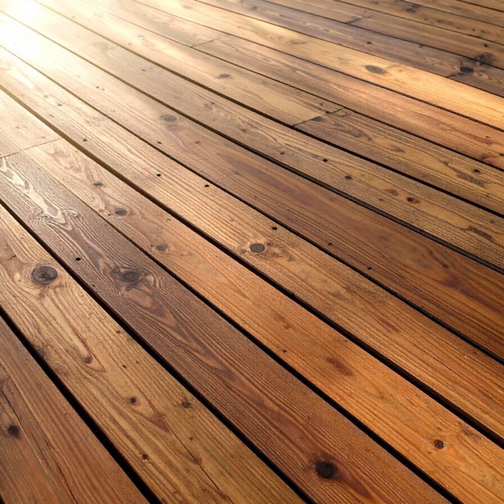 A high-angle view of parallel wooden deck planks with visible grain, knots, and warm brown tones under sunlight.